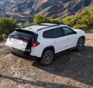 Rear view of a white 2026 GMC Acadia parked on a mountain trail with its liftgate open